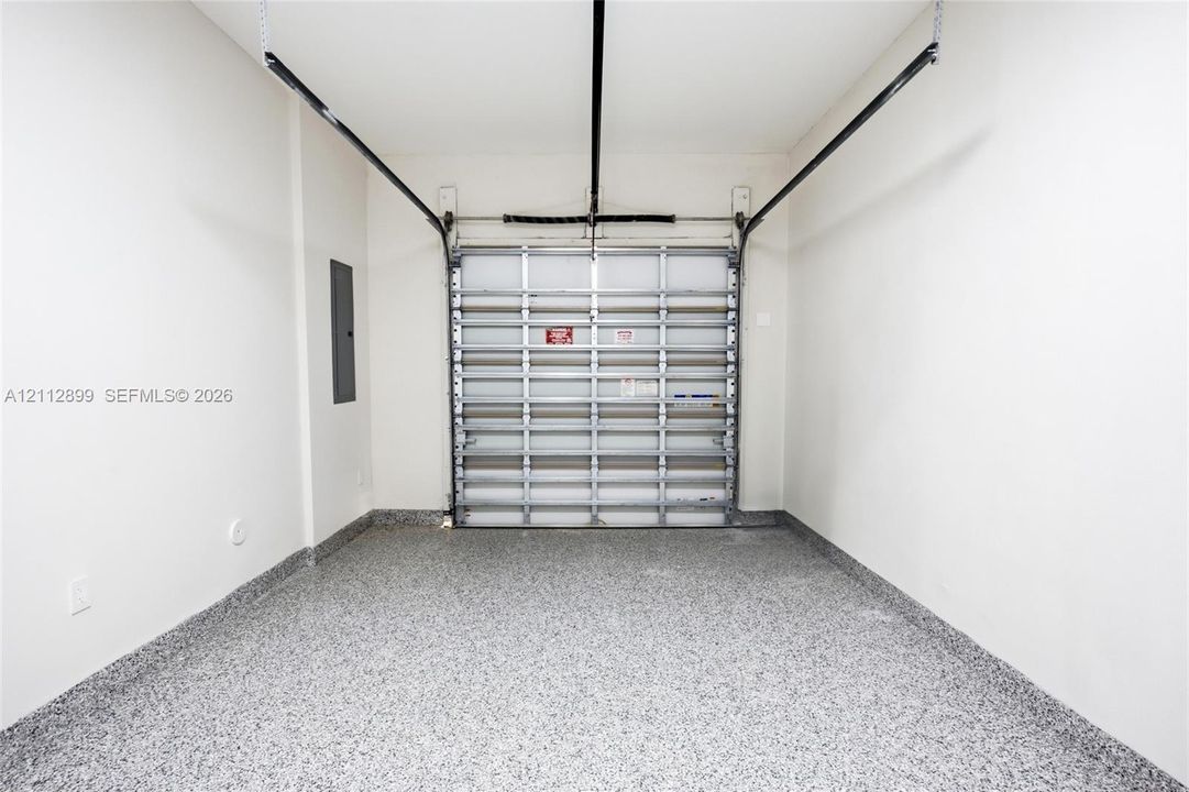 Enclosed garage space featuring a metal overhead door, seamless speckled epoxy flooring, and crisp white wall finishes