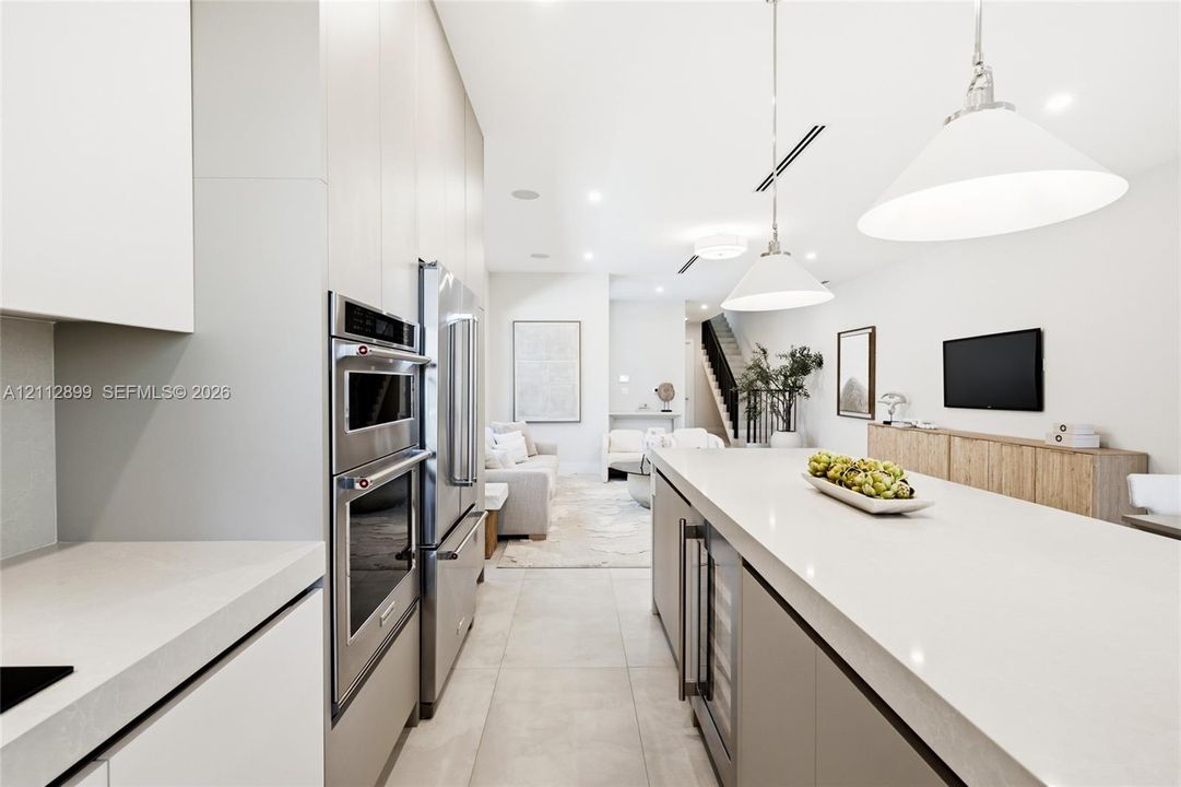 Kitchen featuring flat-panel cabinetry, a spacious island with a solid surface countertop, stainless steel double wall ovens, a side-by-side refrigerator, and large-format tile flooring