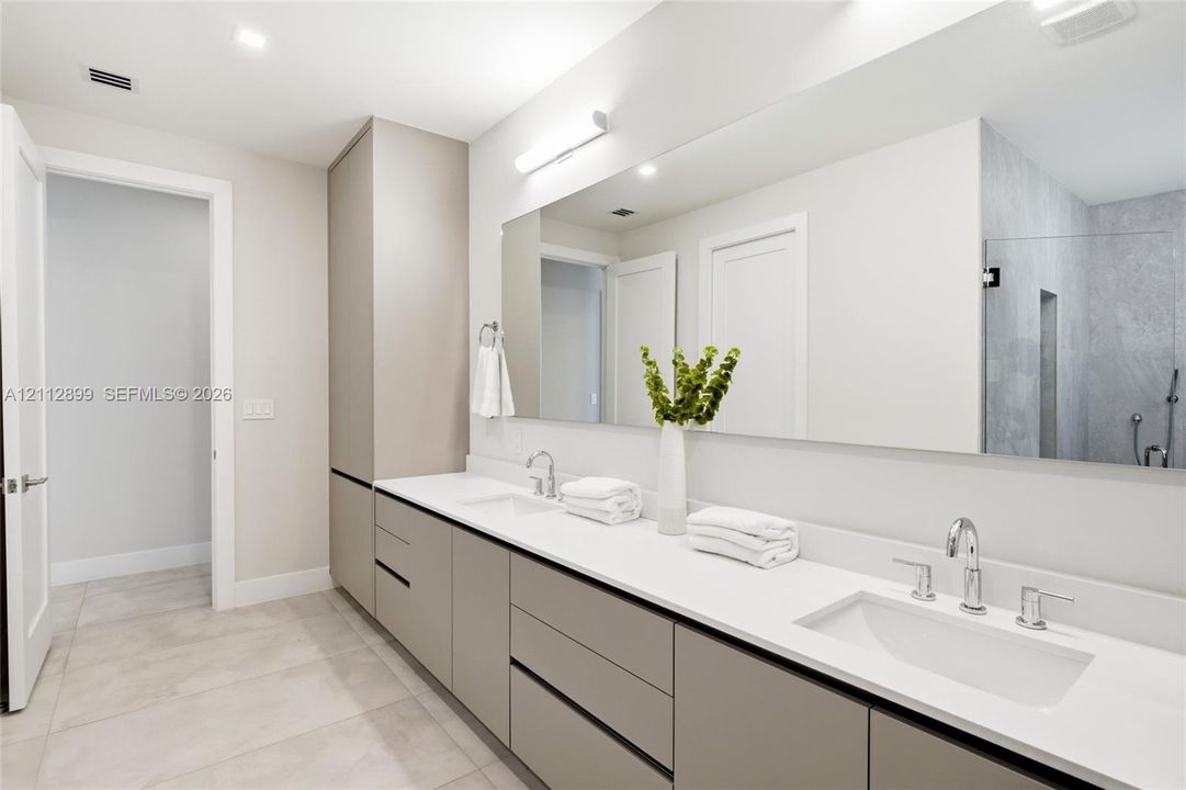 Extended vanity featuring flat-panel cabinetry, light-toned solid surface countertops, dual undermount sinks, and a large-format vanity mirror with integrated linear lighting