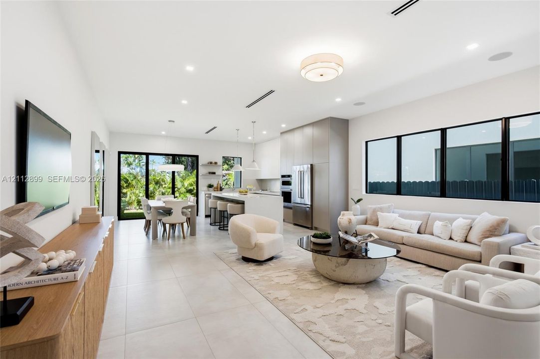 Open-concept interior featuring large-format tile flooring, recessed ceiling lighting, built-in kitchen cabinetry, stainless steel appliances, and black-framed windows