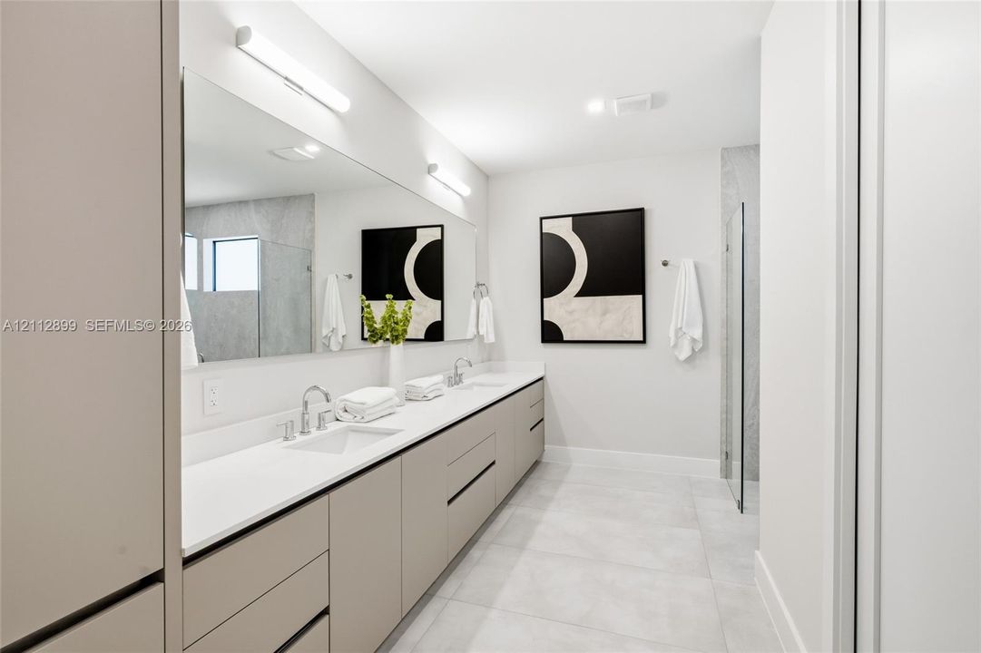 Extended floating vanity with dual undermount sinks, quartz countertop, full-width mirror, and walk-in shower with glass enclosure
