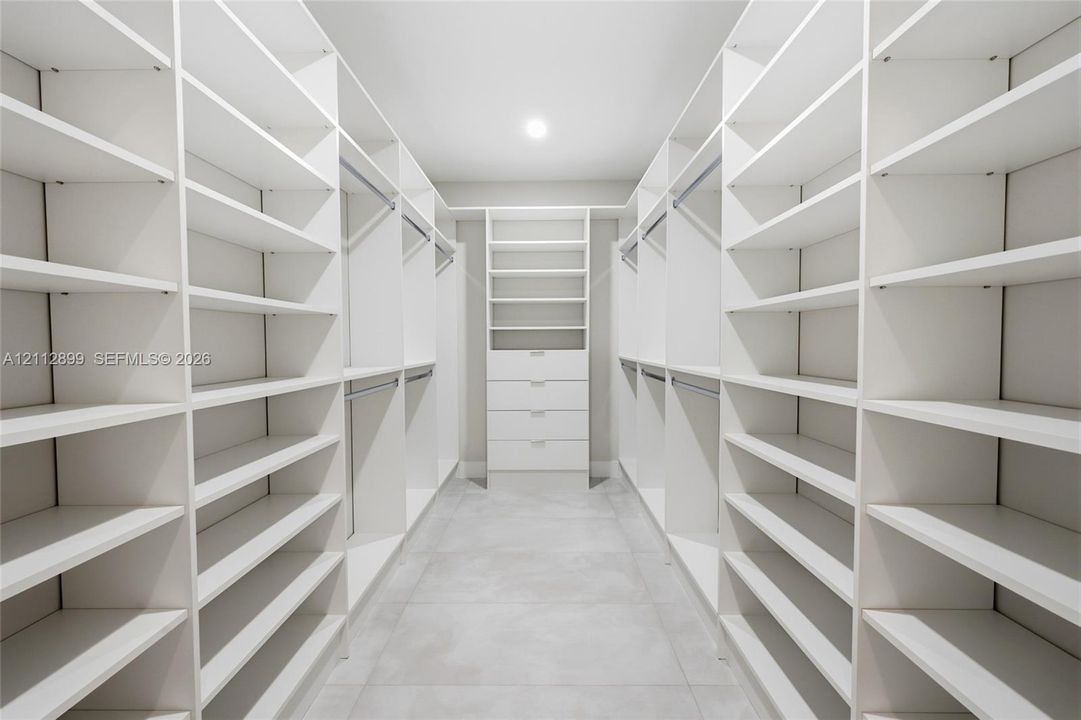 Walk-in closet featuring extensive built-in white shelving, integrated clothing rods, a central drawer bank, and tile flooring