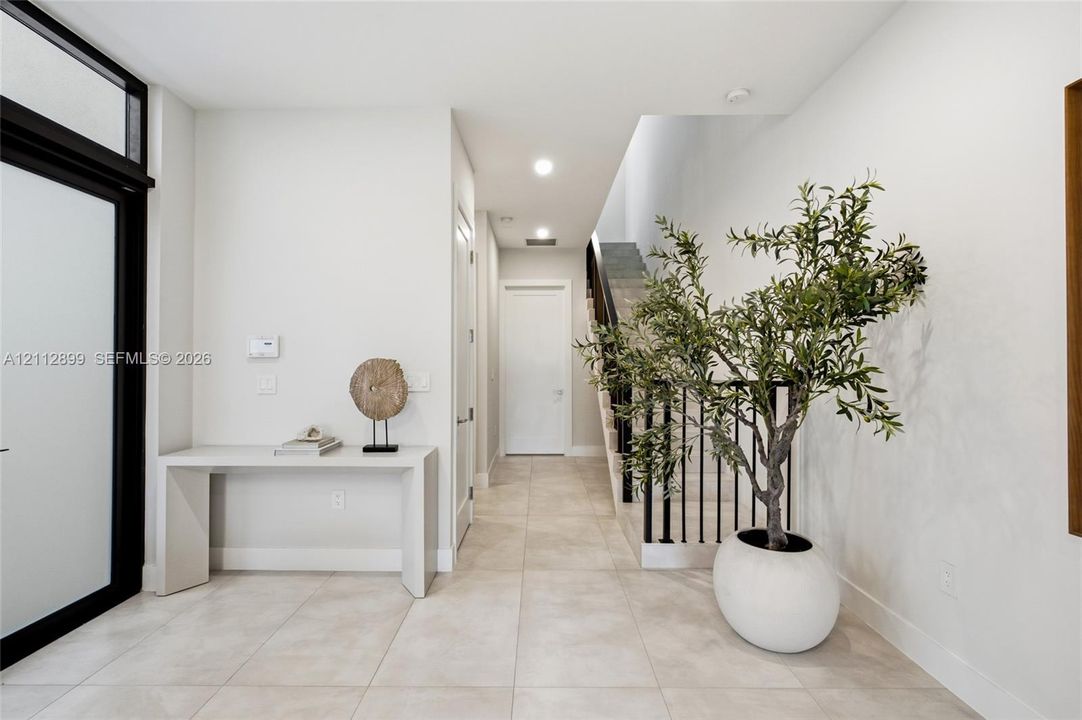 Entryway featuring large-format tile flooring, a glass-paneled front door with black trim, recessed lighting, and a staircase with black metal balusters