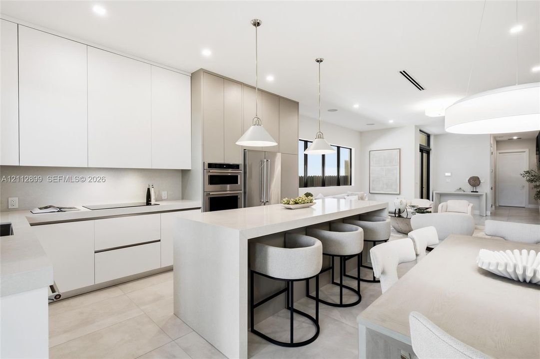 Kitchen featuring floor-to-ceiling cabinetry, a waterfall-edge center island, stone countertops, recessed lighting, and stainless steel built-in double wall ovens