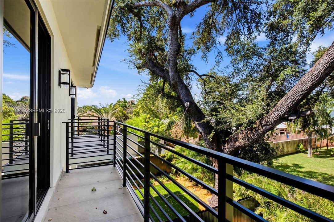 Covered balcony featuring matte black metal railings, concrete flooring, and wall-mounted exterior lighting