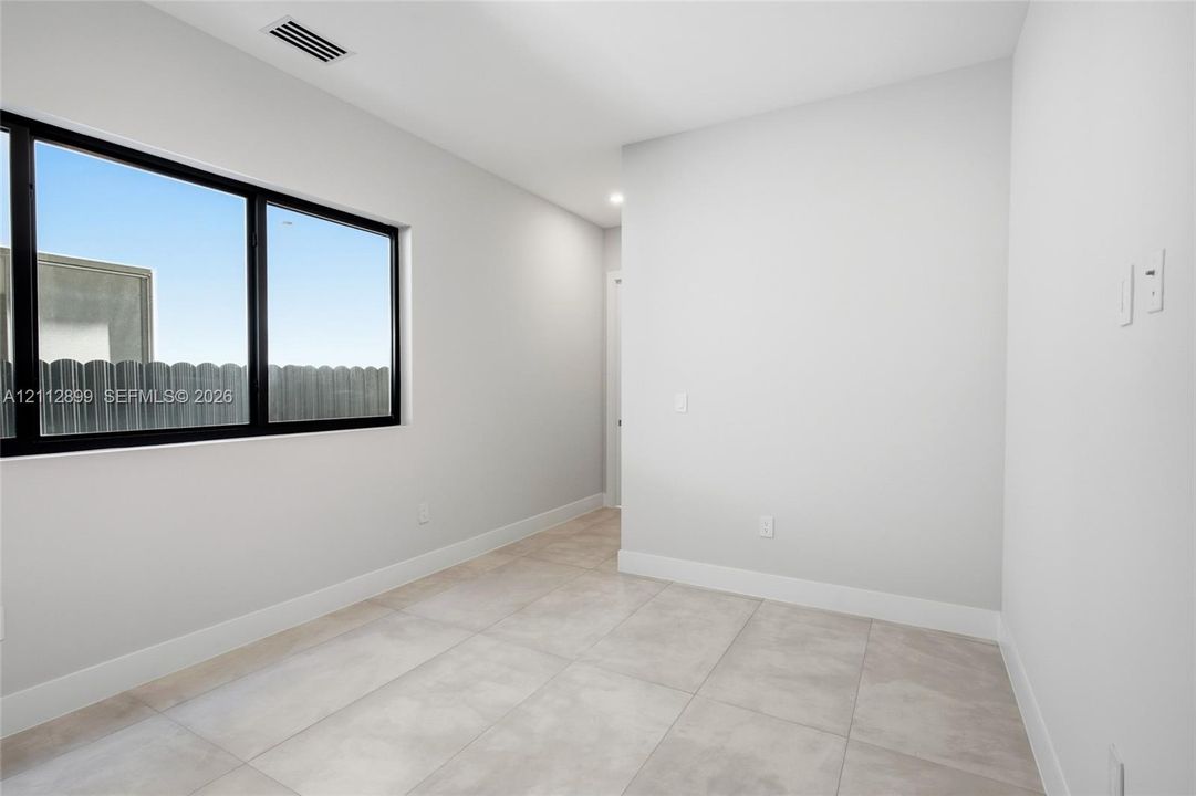 Neutral-toned tile flooring, oversized window with black frame, and smooth-finish walls