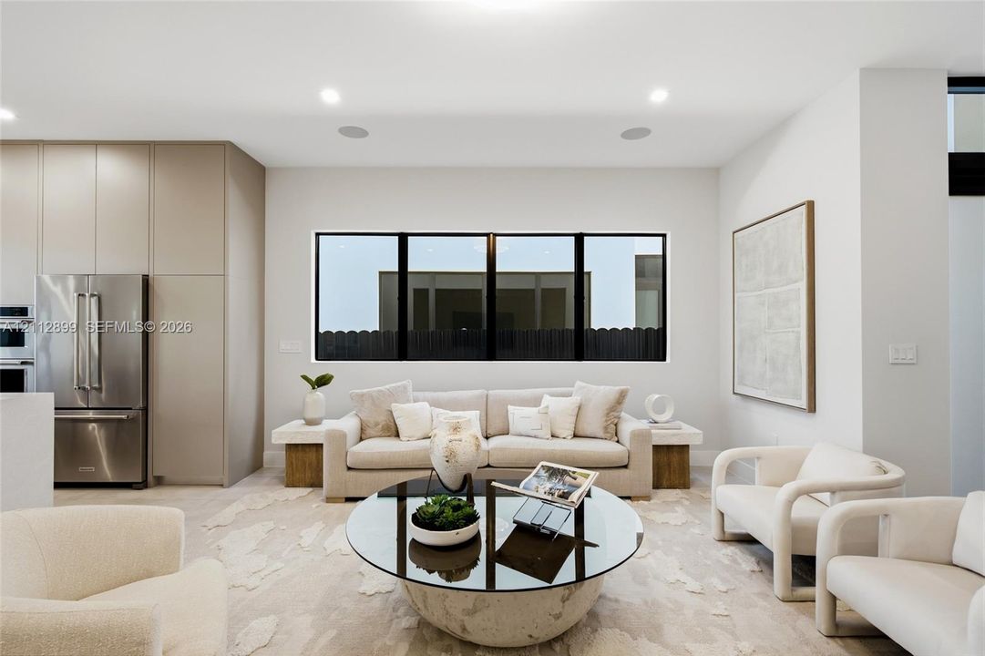 Open-concept living space featuring floor-to-ceiling cabinetry, stainless steel refrigerator, recessed lighting, and expansive tripartite black-framed window