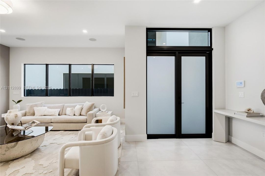 Double entry doors with frosted glass panels and an overhead transom window, large-format tile flooring, recessed lighting, and a built-in wall-mounted console