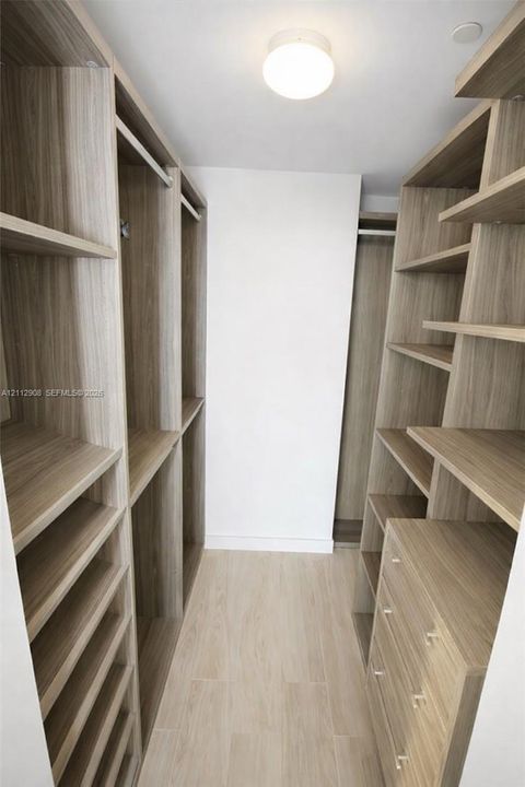 Custom walk-in closet featuring extensive wood-finish built-in shelving, integrated hanging rods, a built-in drawer unit, and wood-finish flooring