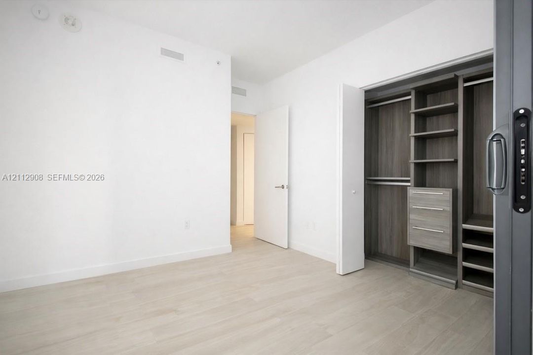 Wood-finish flooring, white interior walls, and built-in closet organization featuring shelving and drawers