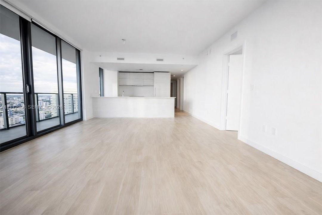 Open-concept interior featuring floor-to-ceiling glass panel walls, wood-finish flooring, and a kitchen with white cabinetry and a flat-surface breakfast bar