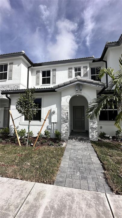 Two-story exterior featuring white stucco finish, stacked stone veneer accents, arched covered entryway, and decorative window shutters