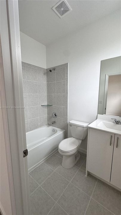 Bathroom featuring a vanity with integrated sink, ceramic tile flooring, bathtub and shower combination with tiled surround, and a wall-mounted mirror