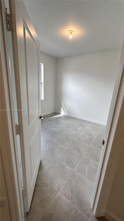 Interior space featuring large-format ceramic tile flooring, neutral wall finishes, a single-panel interior door, and a flush-mount ceiling light fixture