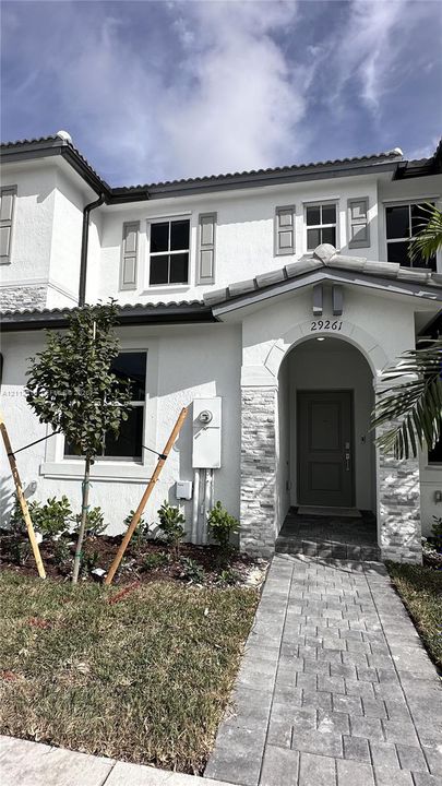 Two-story exterior featuring white stucco finish, stone veneer accents, arched covered entryway, shutter-framed windows, and paved walkway