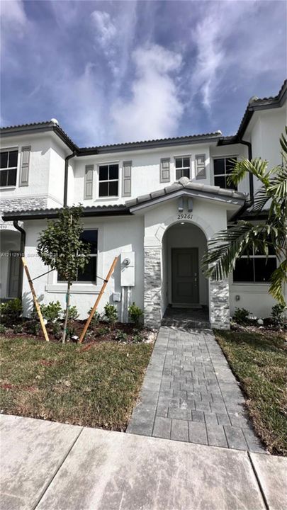 Stucco exterior featuring stacked stone accents, arched entryway, paved stone walkway, and window shutters