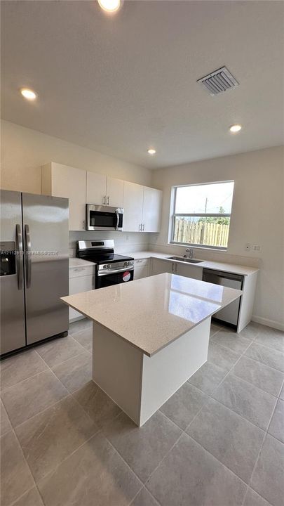 Kitchen featuring a central island with a solid surface countertop, white cabinetry, stainless steel appliances, and large-format tile flooring