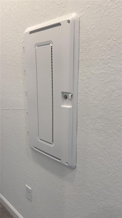 Recessed media distribution panel with a vented white cover and secure locking mechanism mounted on a neutral-toned wall