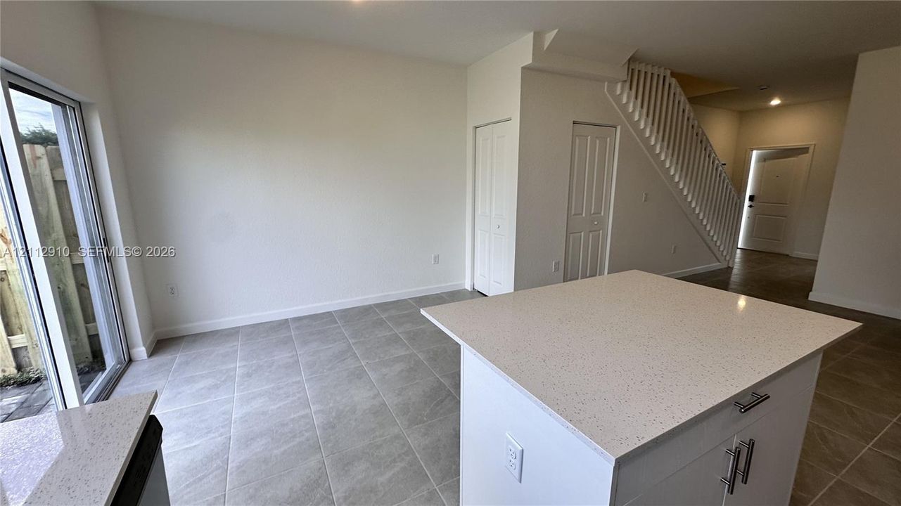 Kitchen island with stone-composite countertop, porcelain tile flooring, sliding glass door, and staircase featuring a vertical balustrade