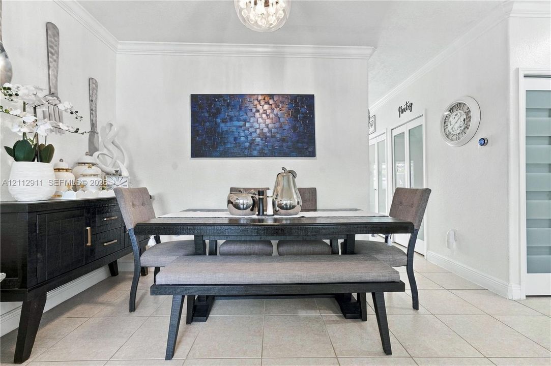 Dining area featuring neutral tile flooring, crown molding, and a spherical glass-shade pendant light