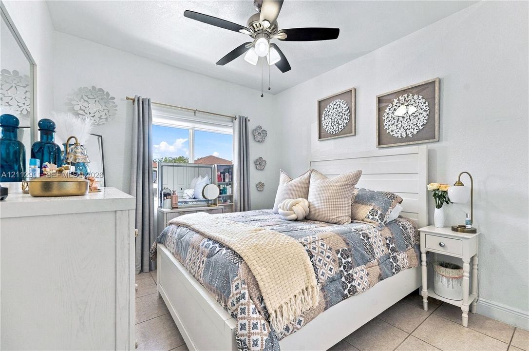 Bedroom featuring light-toned tile flooring, a multi-blade ceiling fan with integrated lighting, and a window with horizontal blinds
