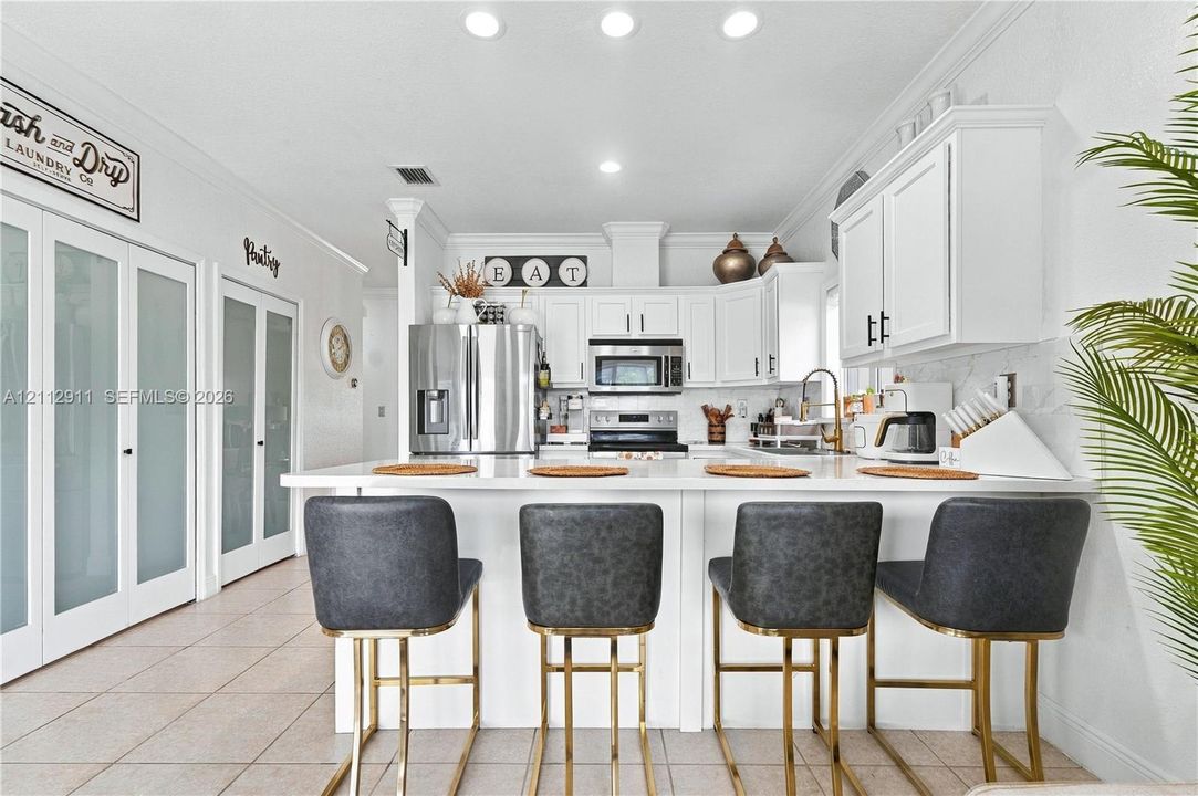 Kitchen featuring white cabinetry, solid-surface countertops, stainless steel appliances, recessed lighting, and dual frosted-glass pantry doors