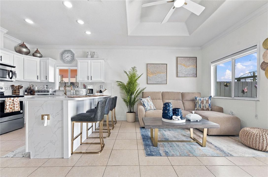 Open-concept kitchen featuring white shaker-style cabinetry, an island with a stone-finish countertop, recessed lighting, and a tray ceiling with a center-mounted ceiling fan