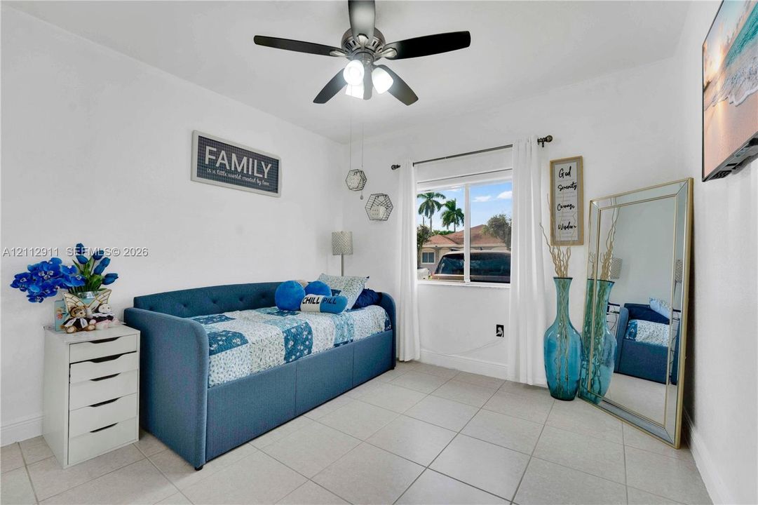 Neutral-toned tile flooring, multi-blade ceiling fan with integrated light fixture, and single-pane sliding window