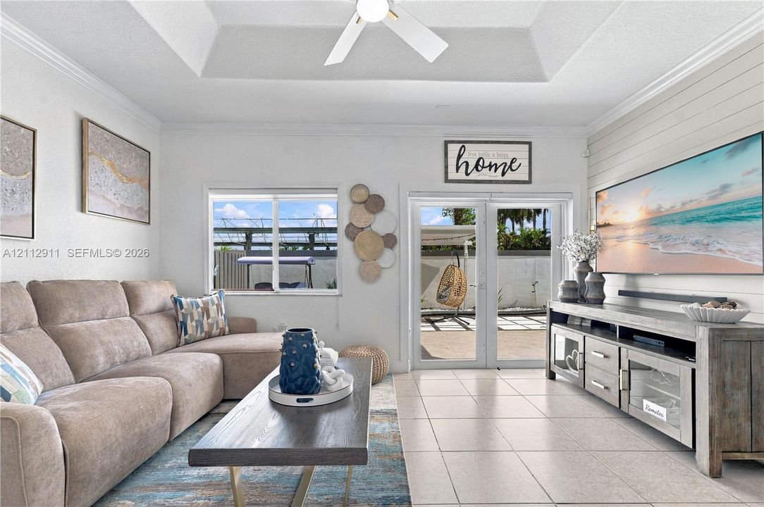Living area featuring a tray ceiling with a recessed ceiling fan, horizontal shiplap wall accent, tile flooring, and double glass doors providing exterior access