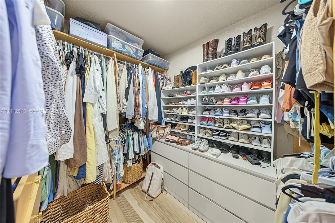 Walk-in closet featuring extensive built-in shelving, multi-level hanging rods, integrated drawer storage, and wood-finish flooring