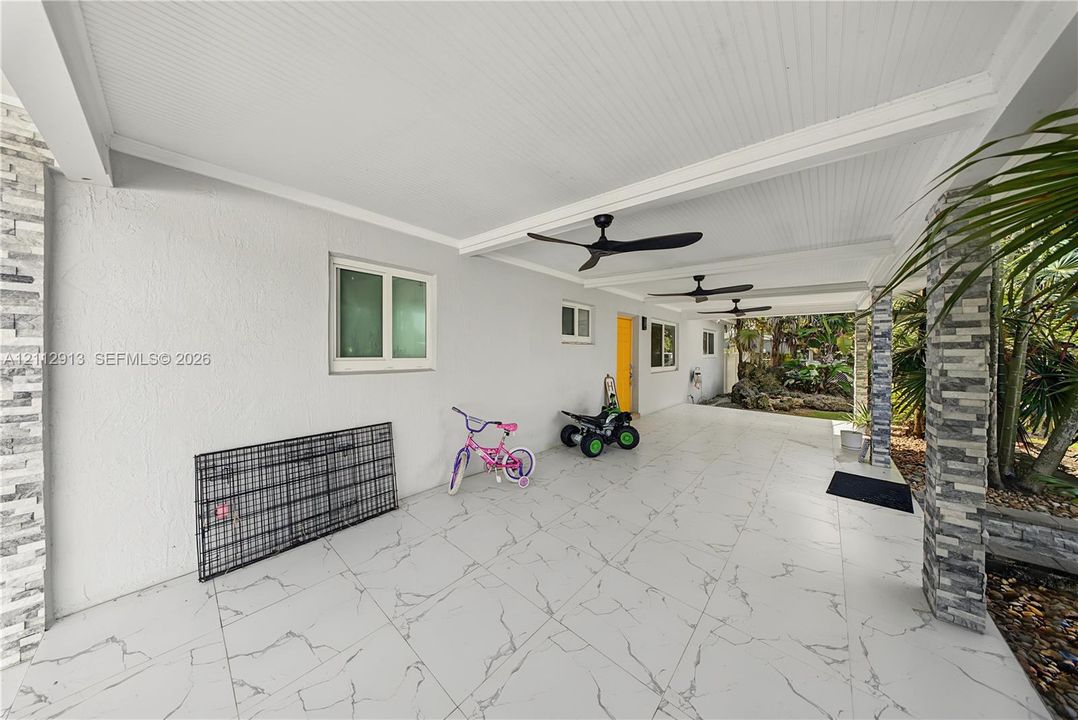 Covered patio featuring large-format stone-finish tile flooring, beadboard ceiling, stacked stone structural columns, and dual ceiling fans