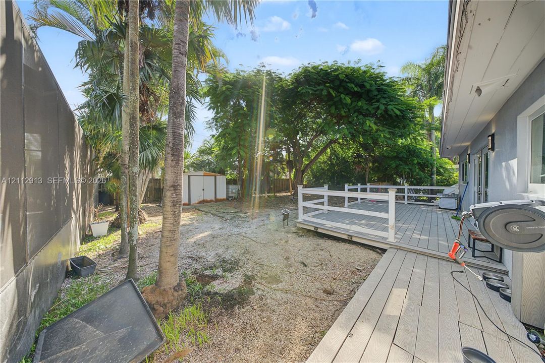 Backyard featuring a raised wooden deck with white railing, mature palm trees, and a detached storage shed