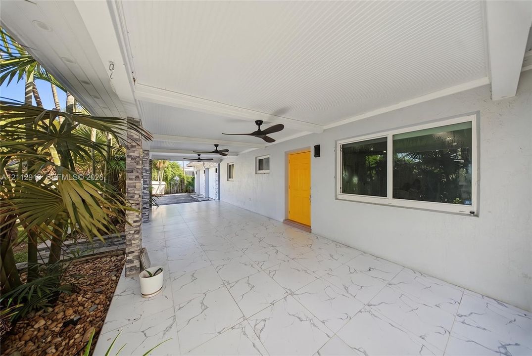 Covered exterior patio featuring large-format stone-finish tile flooring, beadboard ceiling, multiple ceiling fans, and a stone-clad support pillar