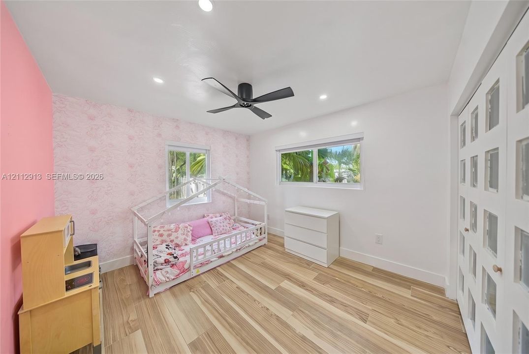 Interior room featuring wood-finish flooring, recessed lighting, matte black ceiling fan, dual windows, and closet doors with glass panel inserts