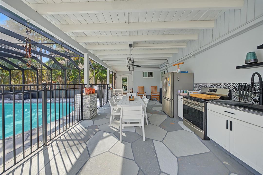 Covered lanai featuring a pool enclosed by aluminum screening, patterned tile backsplash, stone-cladding pillar accents, and concrete paver-style flooring