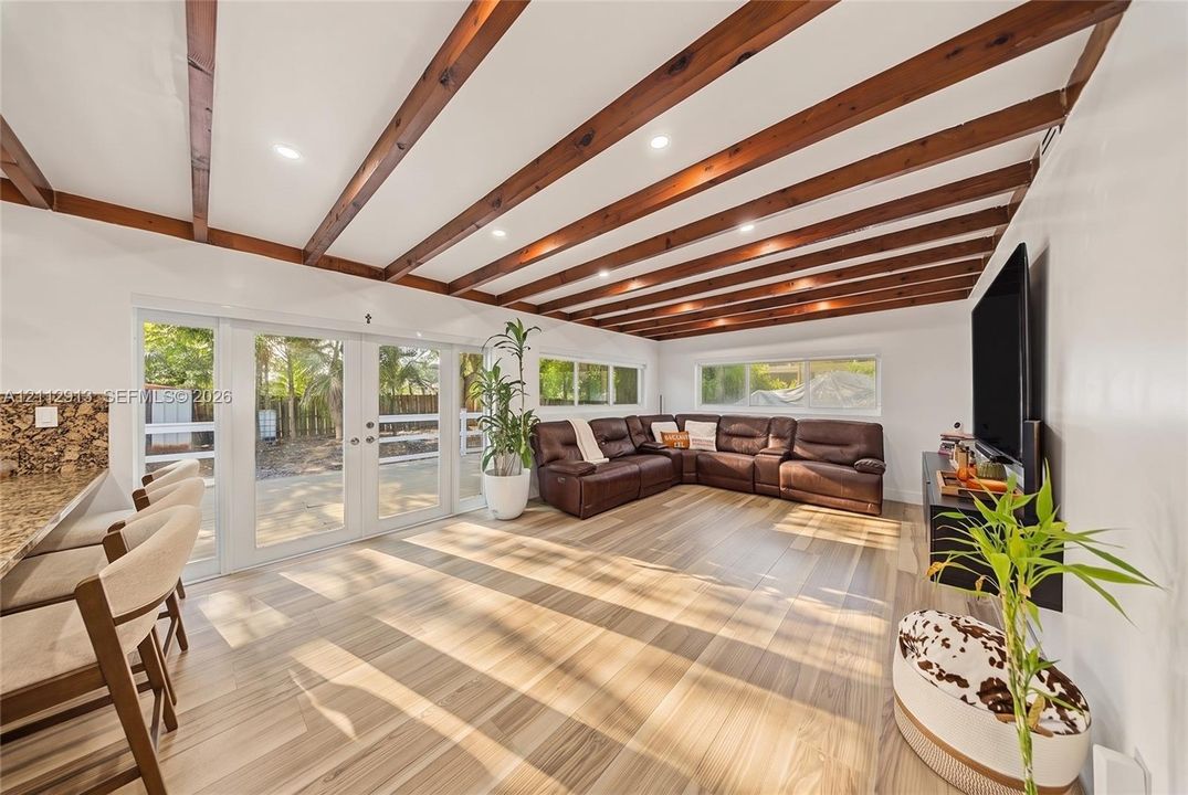 Living space featuring wood-finish flooring, exposed wood ceiling beams, white walls, large multi-pane glass doors, and recessed ceiling lighting