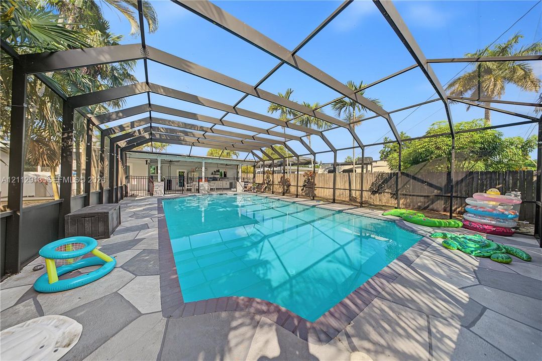 Screened-in pool area featuring geometric stone decking, a brick pool border, and a perimeter wood fence