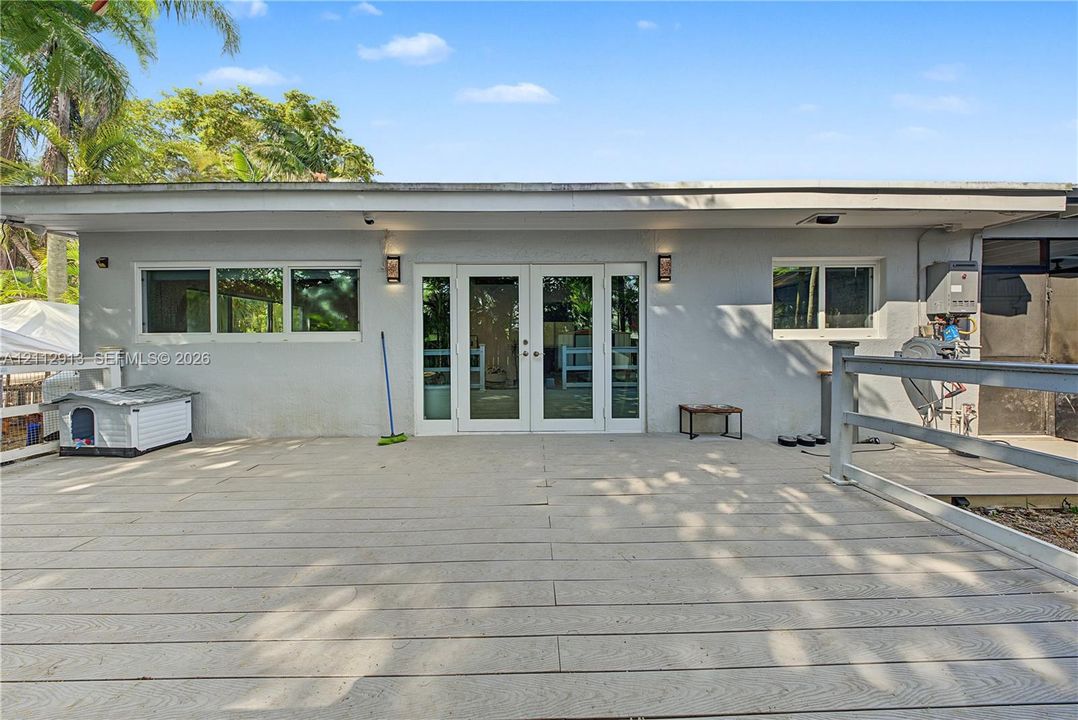 Expansive composite deck featuring perimeter railings, double-glass entry doors, wall-mounted exterior lighting, and aluminum-framed windows