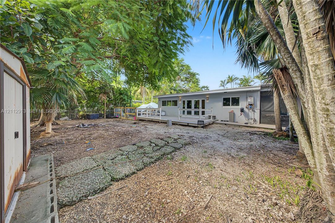 Rear exterior featuring a raised wooden deck with white railing, paved stone path, detached storage shed, and mature trees