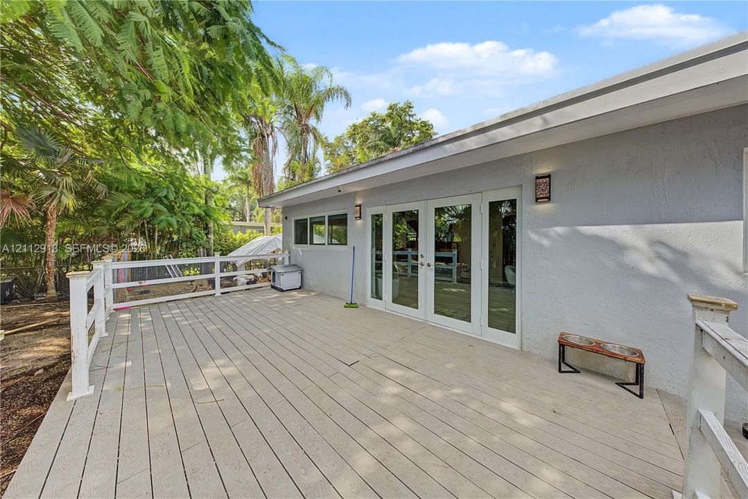 Expansive elevated deck with white railing, double glass-paneled doors, and exterior wall-mounted lighting
