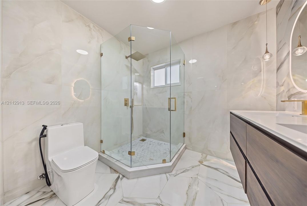 Bathroom featuring full-height stone-finish wall tiling, a walk-in corner shower with gold-tone fixtures and glass enclosure, a floating dual-drawer vanity with white countertop, and large-format porcelain tile flooring