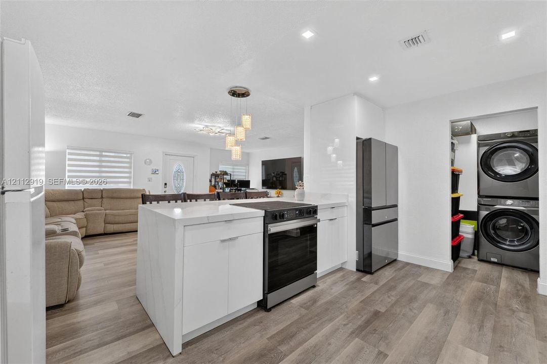Kitchen island featuring a stone countertop, wood-finish flooring, recessed lighting, and a dedicated laundry area with stacked washer and dryer unit