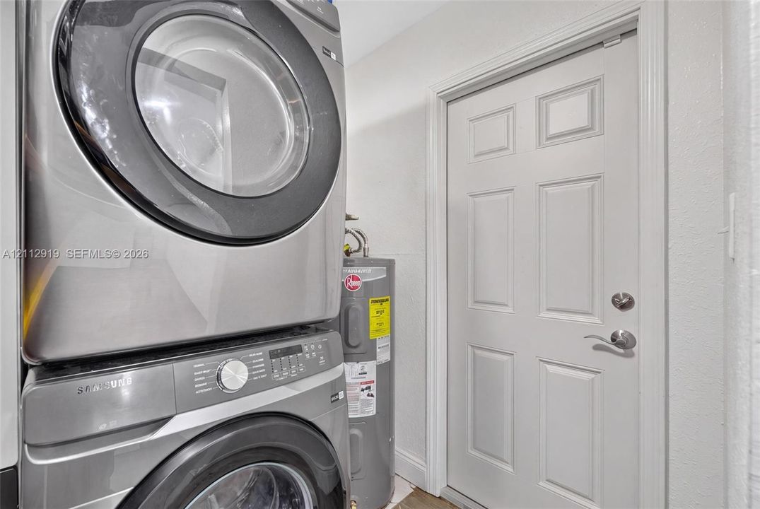 Stacked stainless steel front-load laundry appliances and a vertical water heater paired with a six-panel interior door featuring satin nickel hardware