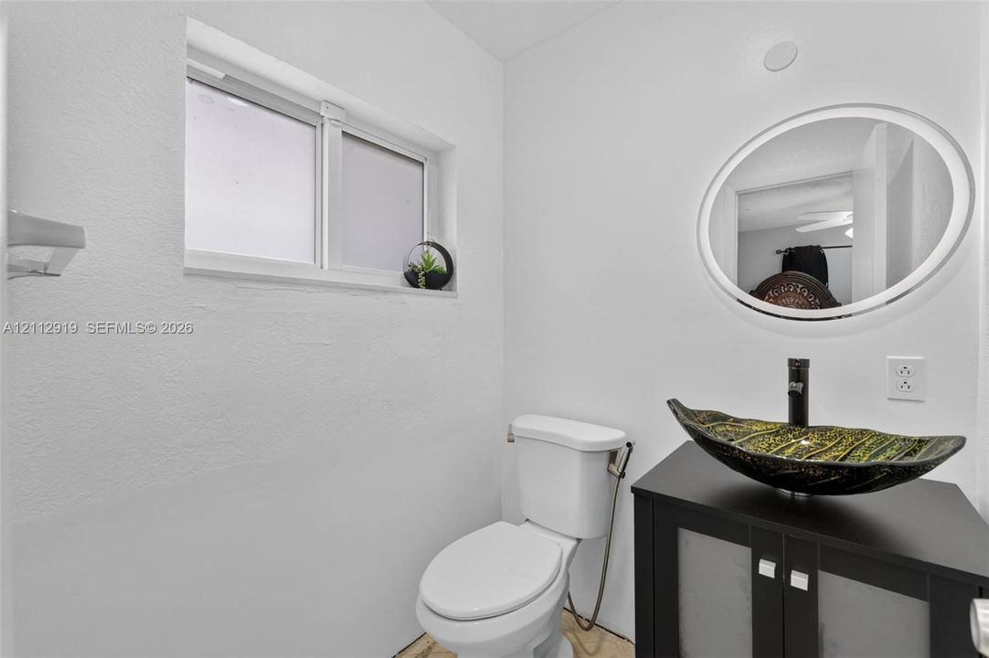 Bathroom featuring a dark wood-finish vanity, decorative vessel sink, black faucet, oval wall mirror, and sliding window