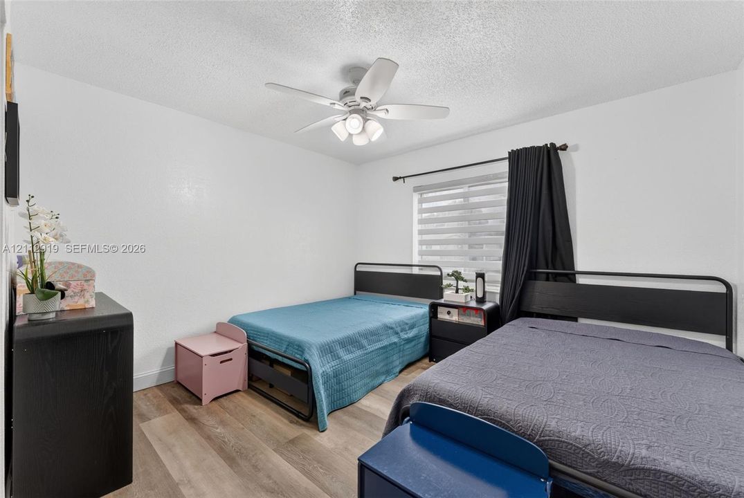 Interior room featuring wood-finish flooring, a ceiling fan with integrated lighting, textured ceiling, a window with horizontal blinds, and a built-in electrical outlet