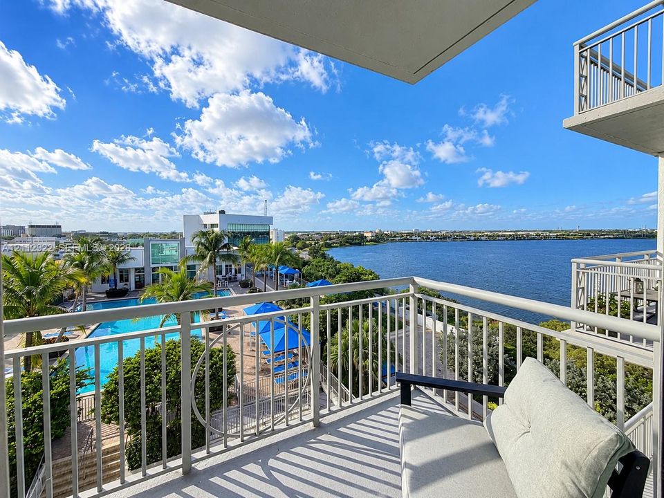 Private balcony featuring metal railings and concrete flooring, overlooking a swimming pool, mature palm trees, and waterfront scenery