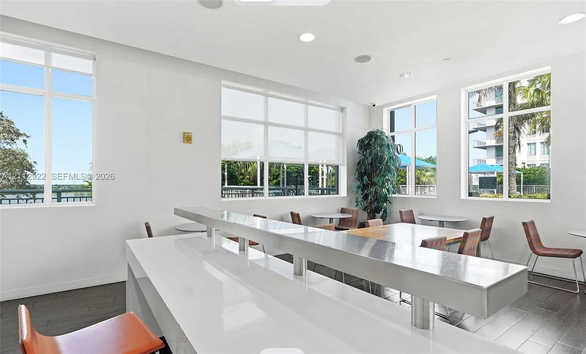 Multi-level tiered island with a white solid-surface countertop, recessed ceiling lighting, wood-finish flooring, and expansive windows with roller shades