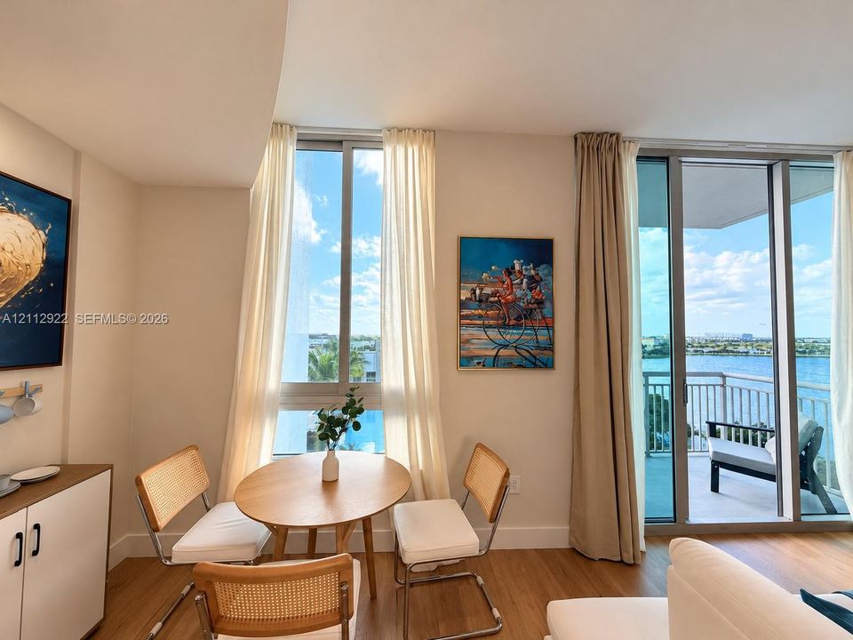 Floor-to-ceiling windows, wood-finish flooring, and a private balcony featuring a water backdrop