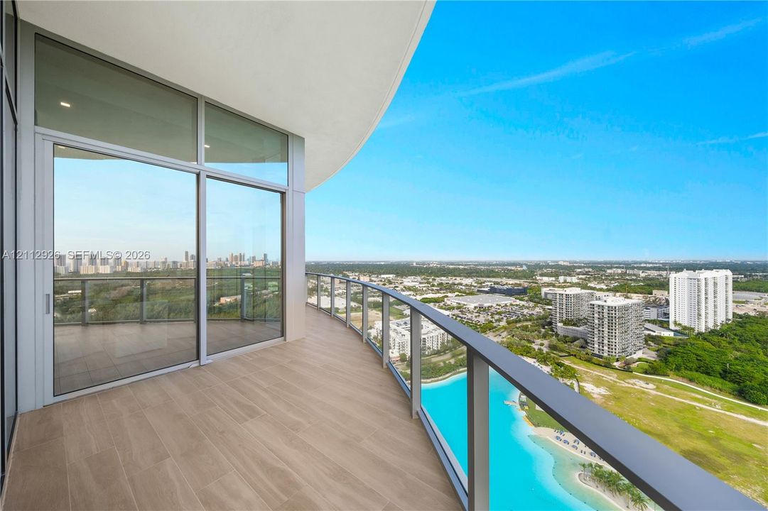 Expansive curved balcony featuring wood-finish tile flooring, a glass panel railing, and floor-to-ceiling glass wall access