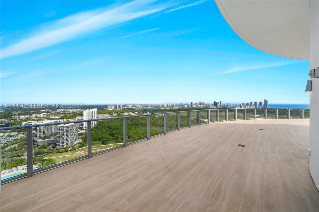 Expansive wrap-around balcony featuring wood-finish tile flooring and a minimalist glass-panel railing